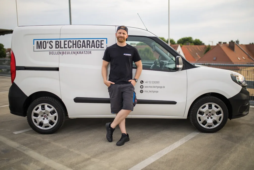 Moritz von Mo's Blechgarage steht vor seinem beschrifteten Servicefahrzeug